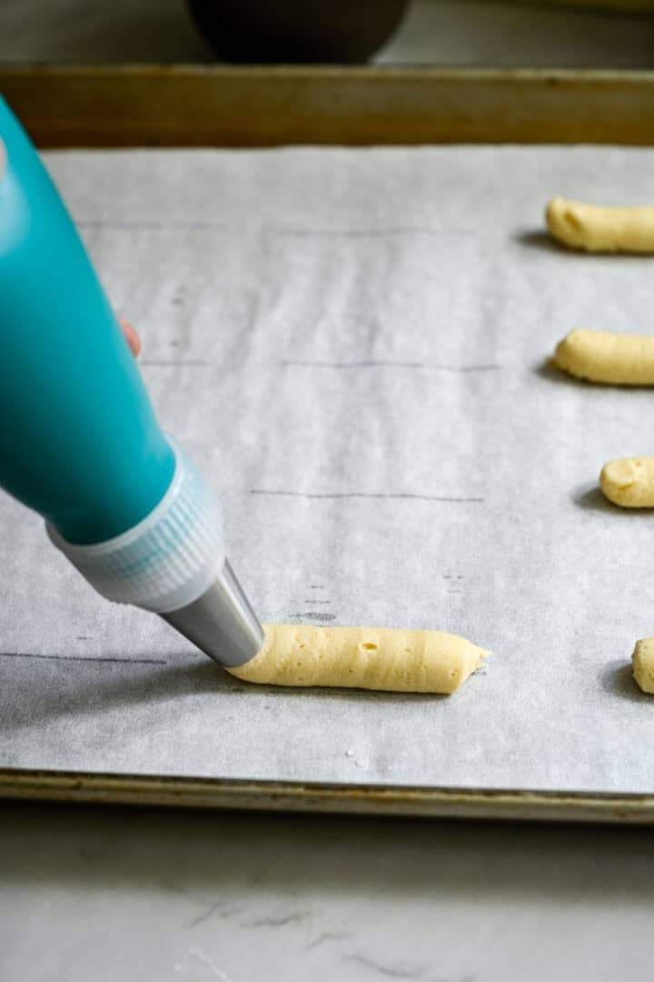 piping cookie dough onto a baking sheet into a straight line.