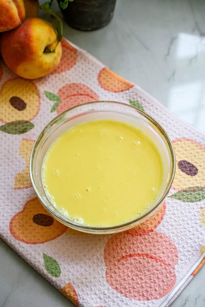 Overhead view of egg yolks and milk tempering in a small glass bowl.