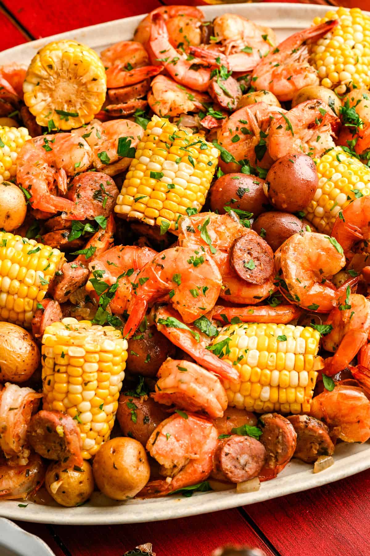 Close up view of sheet pan shrimp boil on a platter with corn, shrimp, sausage and potatoes.