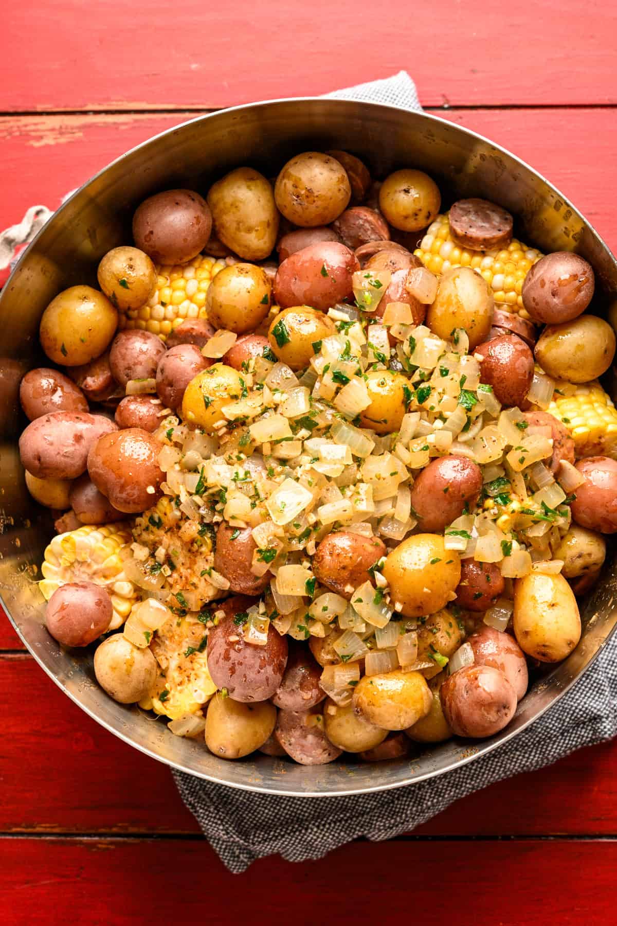 Shrimp, corn, potatoes and sausage in a large bowl with garlic old bay butter sauce poured over the top before mixing.