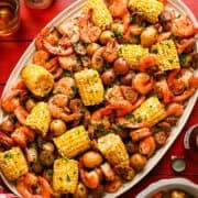 Overhead view of sheet pan shrimp boil on a platter with corn, shrimp, sausage and potatoes.