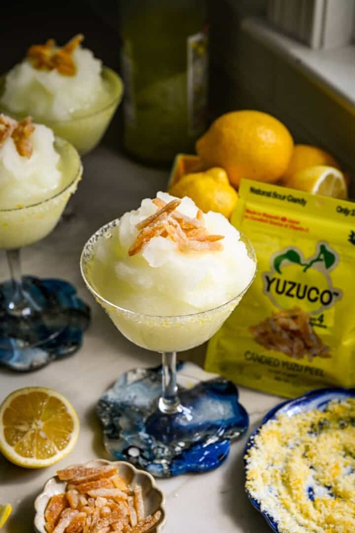 close up view of frozen limoncello cocktail in a coupe glass with candied yuzu peel garnish.