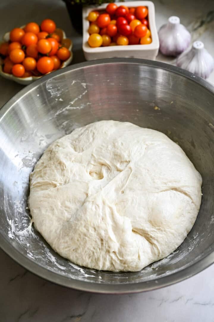 risen focaccia dough in a stainless steel bowl.