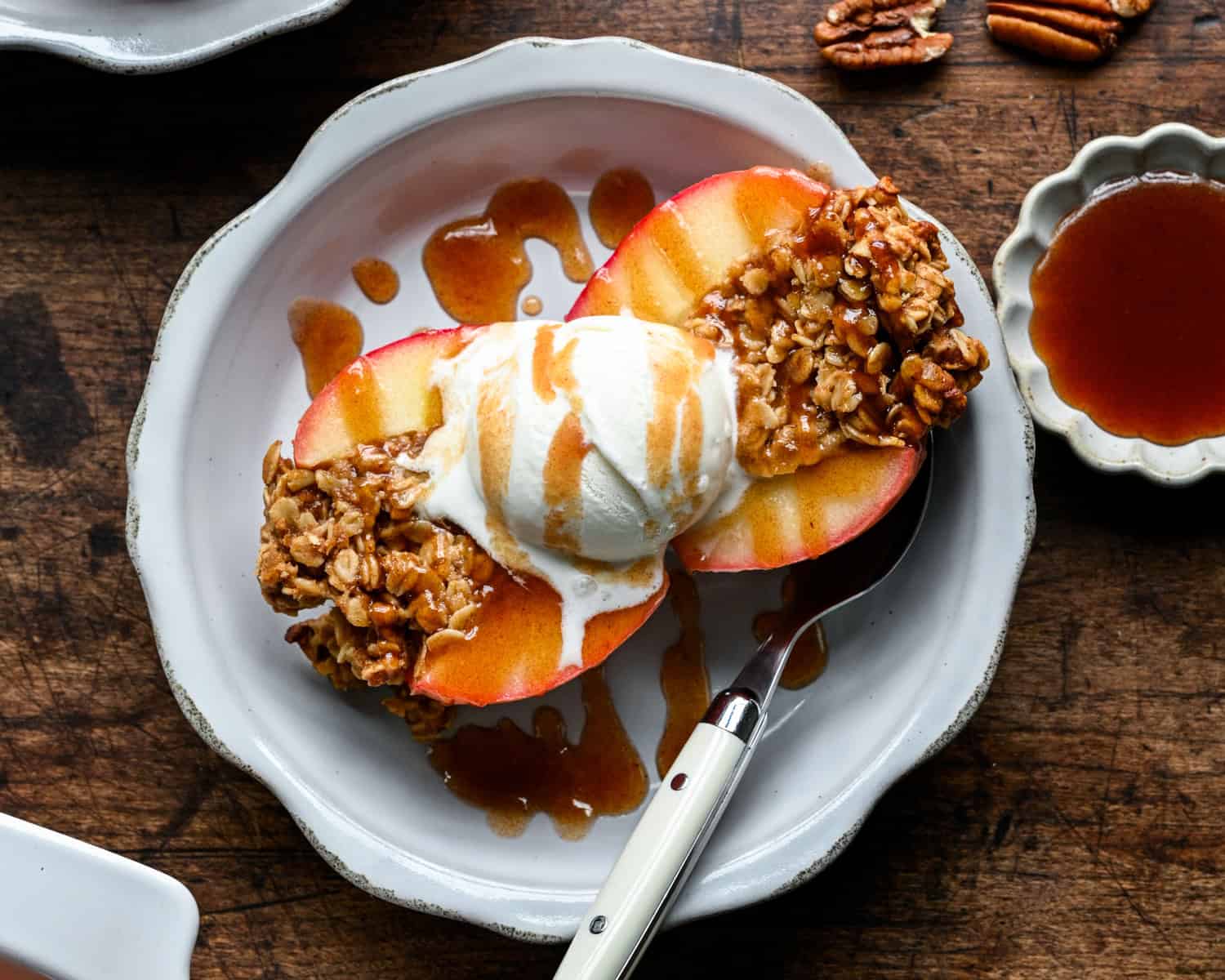 Overhead view of a halved baked apple with melting vanilla ice cream and a drizzle of date caramel, a spoon resting on the plate.