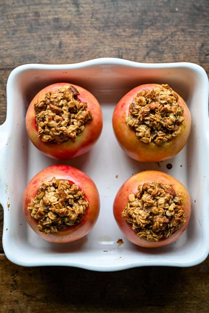 The same four apples after baking, skins softened and wrinkled and the oat topping browned.