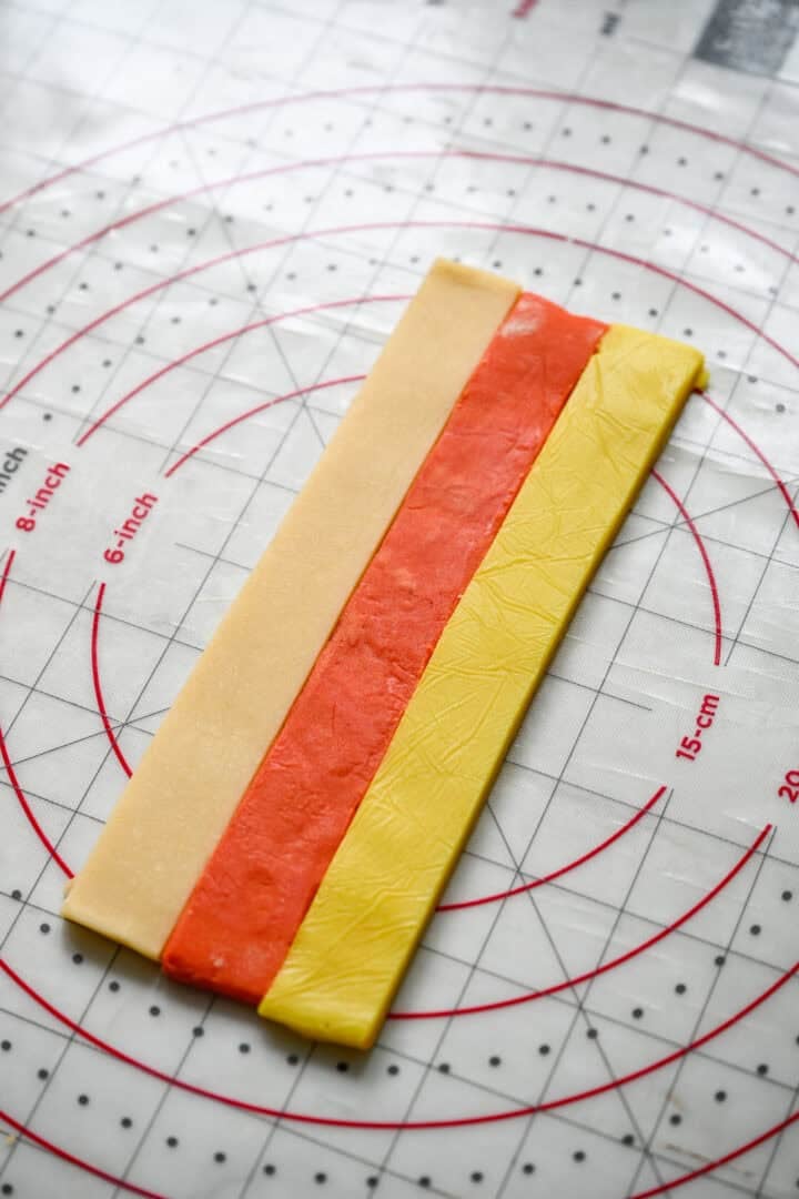 One strip each of plain, orange and yellow dough pressed together edge to edge to form the candy corn stripes.