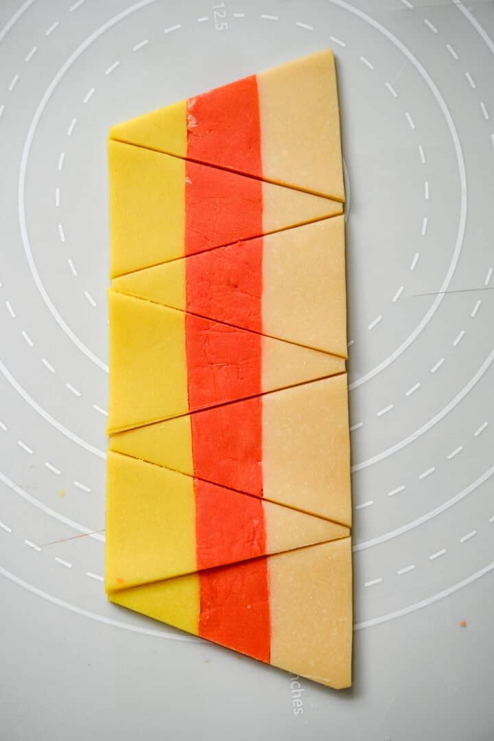 A striped strip of yellow, orange and plain dough cut into alternating candy corn triangles.
