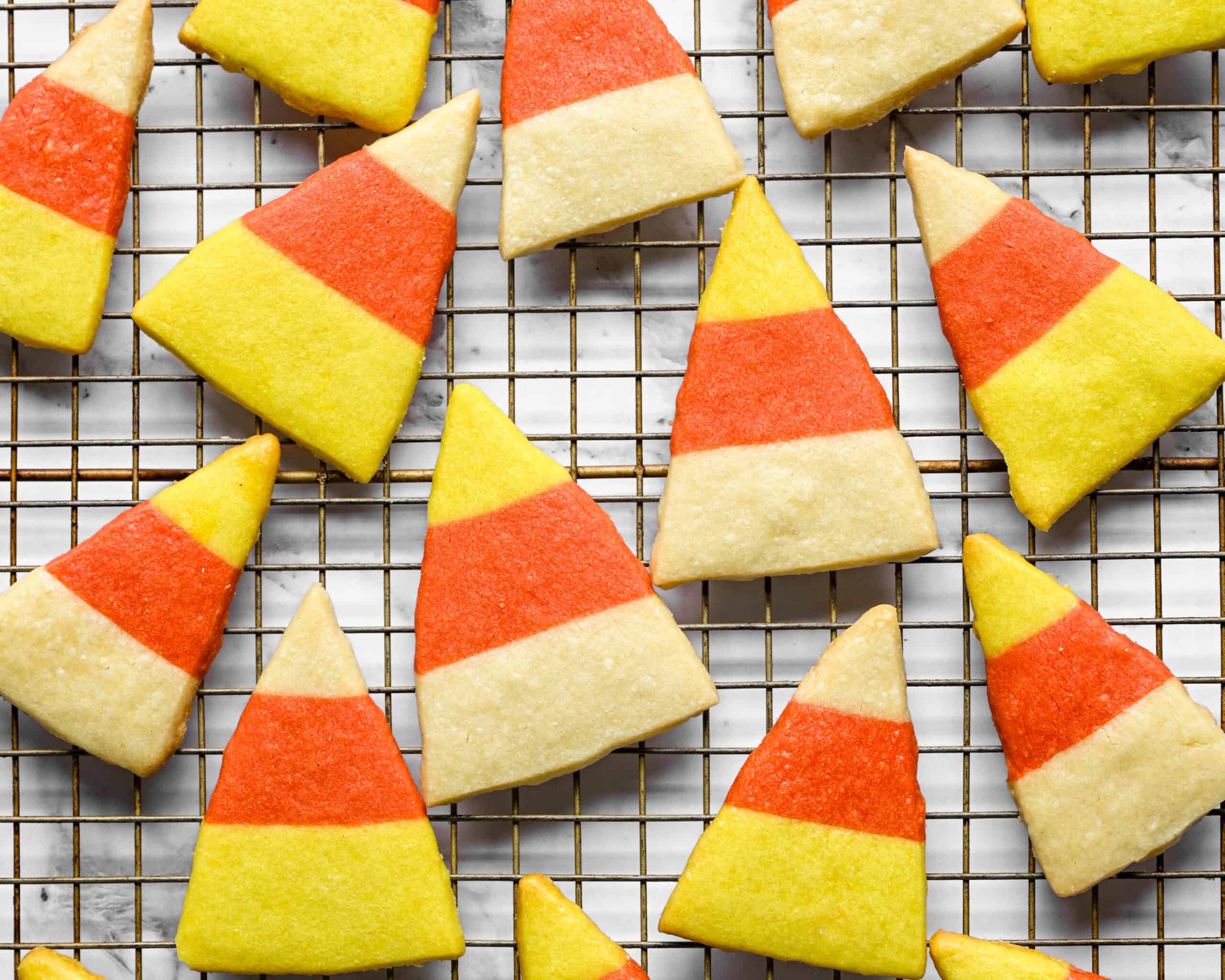Candy corn shortbread cookies with yellow, orange and white stripes cooling on a wire rack.