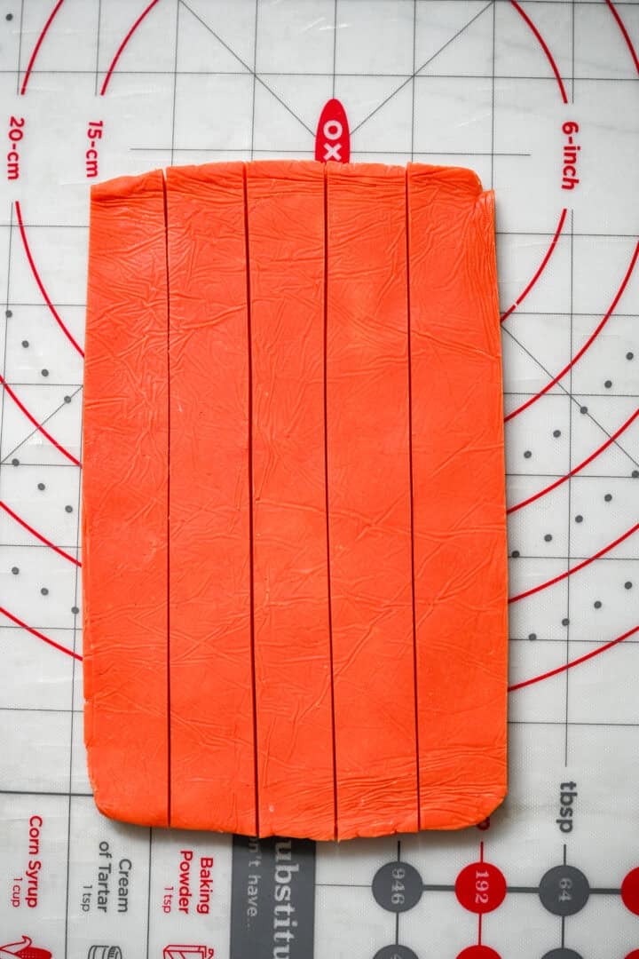 A rectangle of orange dough on a measuring mat, cut lengthwise into five even strips.