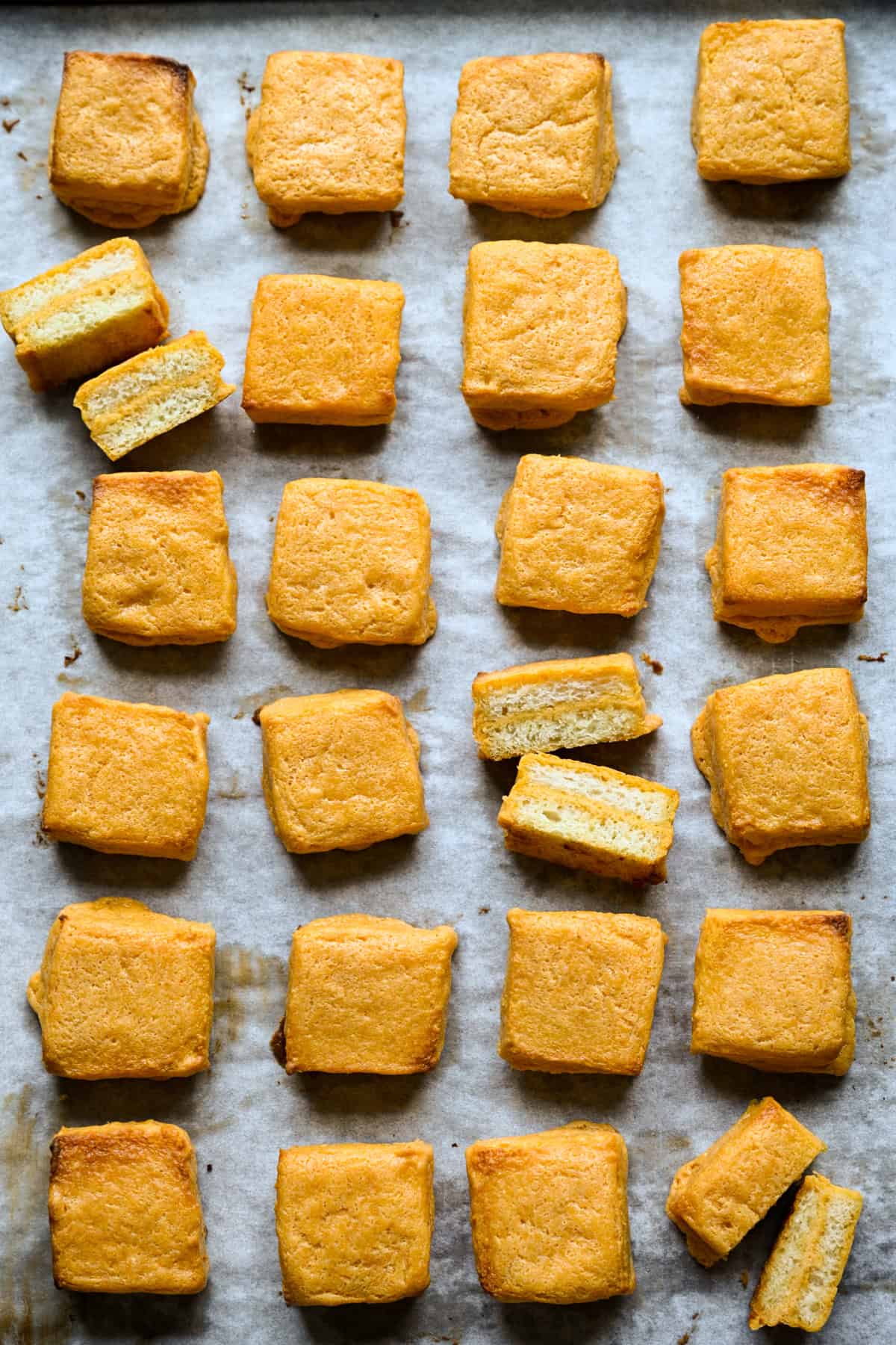 Overhead view of a sheet pan of baked cheese dreams, a few split to show the layers.