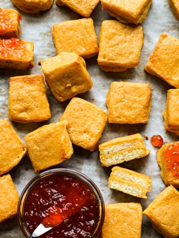 Close up view of cheese dreams beside a jar of red jelly, two of them topped with jelly.