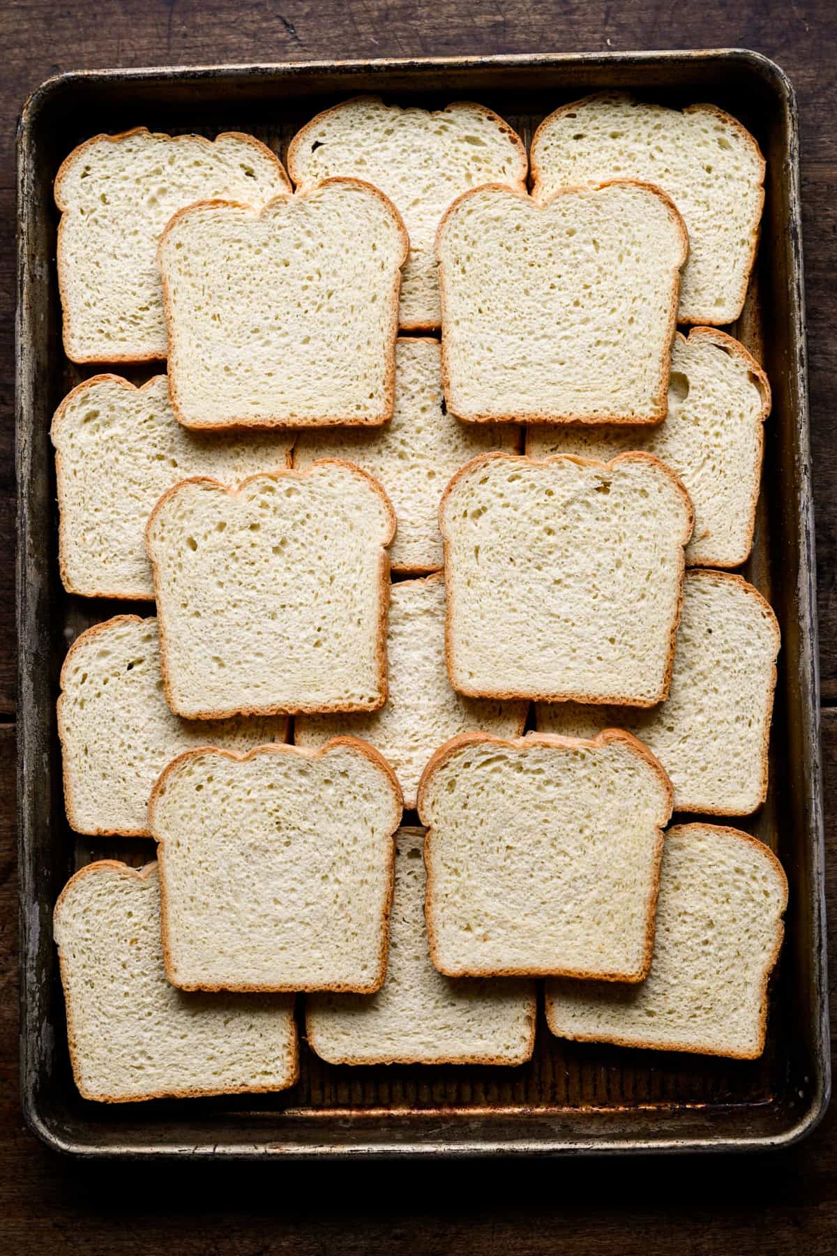 Overhead view of slices of frozen white sandwich bread laid out across a metal sheet pan.