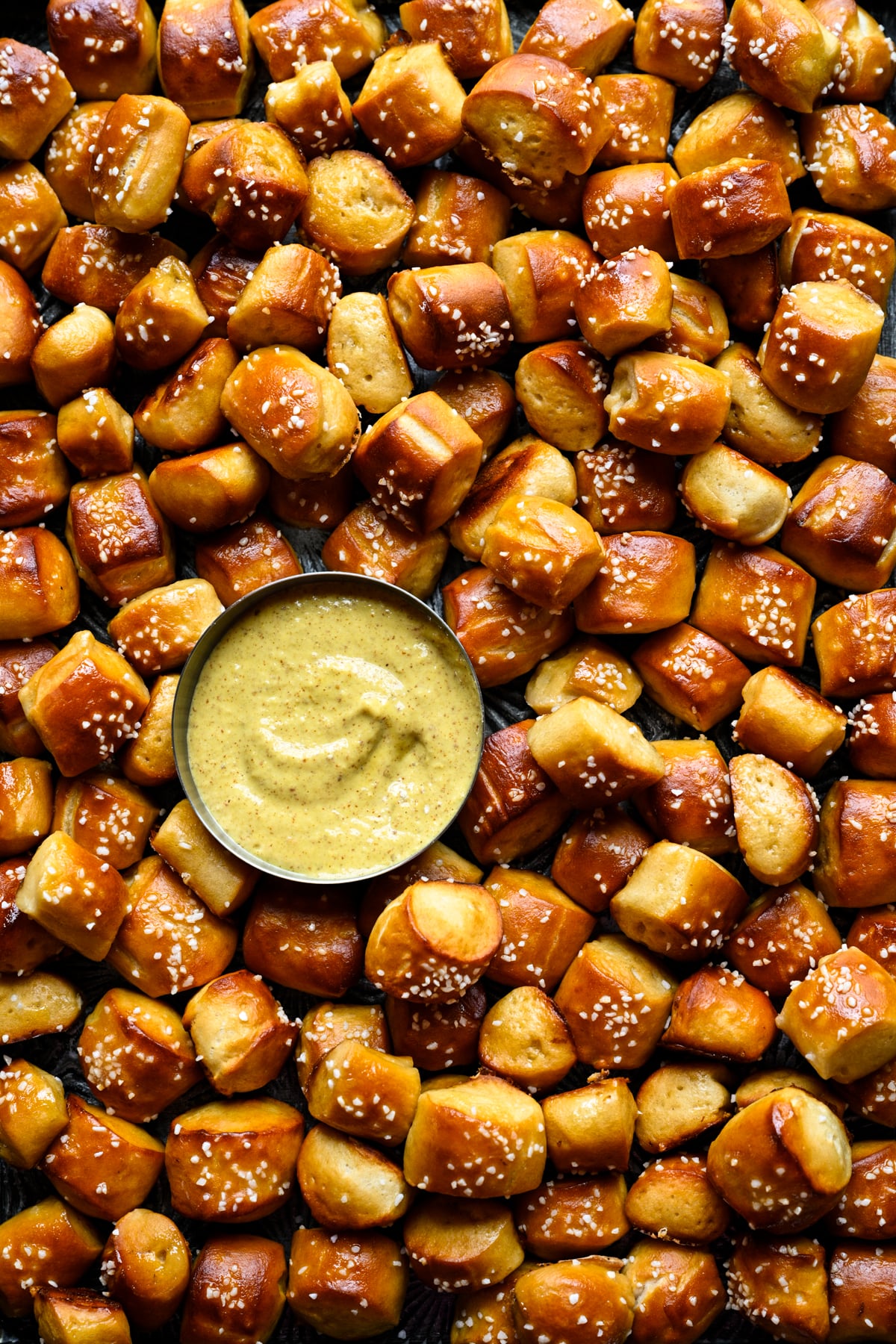 Close overhead view of a pile of buttery soft pretzel bites with pretzel salt surrounding a small bowl of mustard dip.