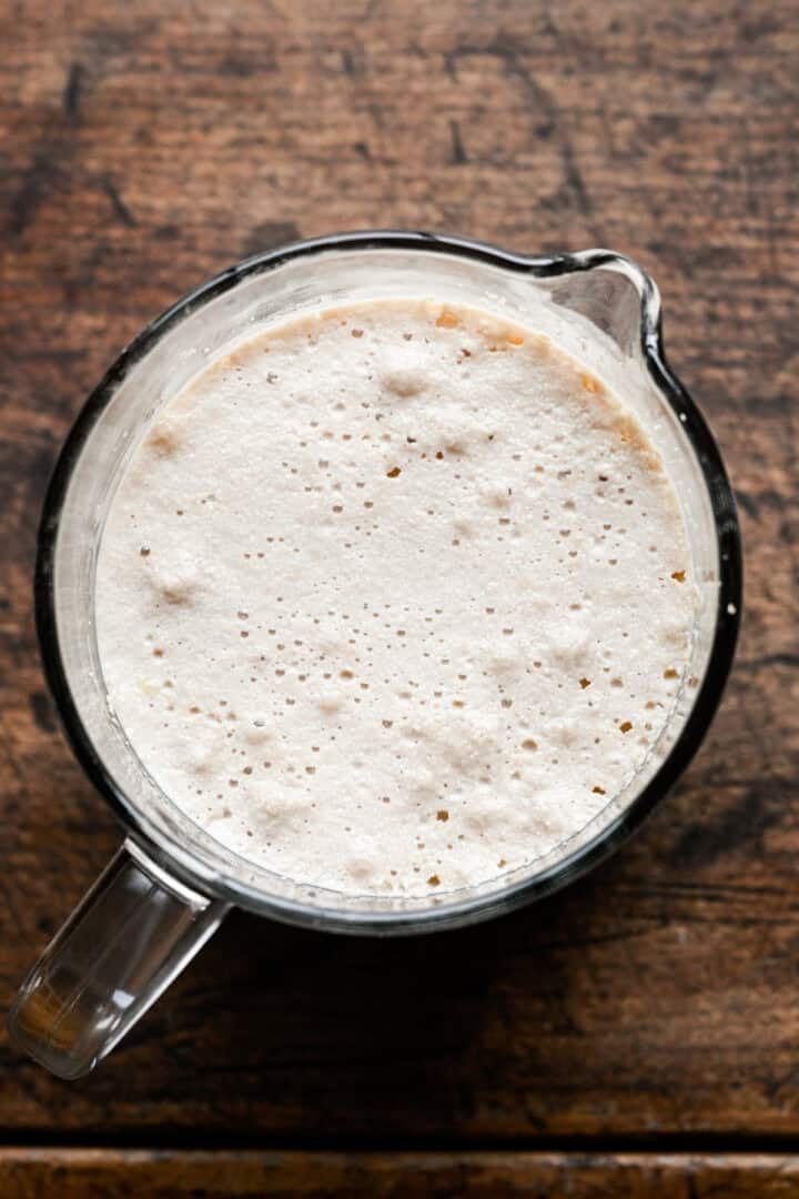 Foamy, bloomed yeast and milk mixture in a glass measuring cup.