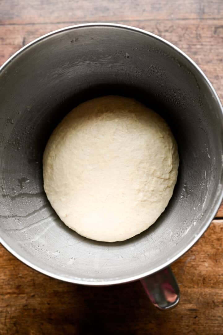 Smooth ball of kneaded pretzel dough in a stainless steel mixing bowl, before rising.