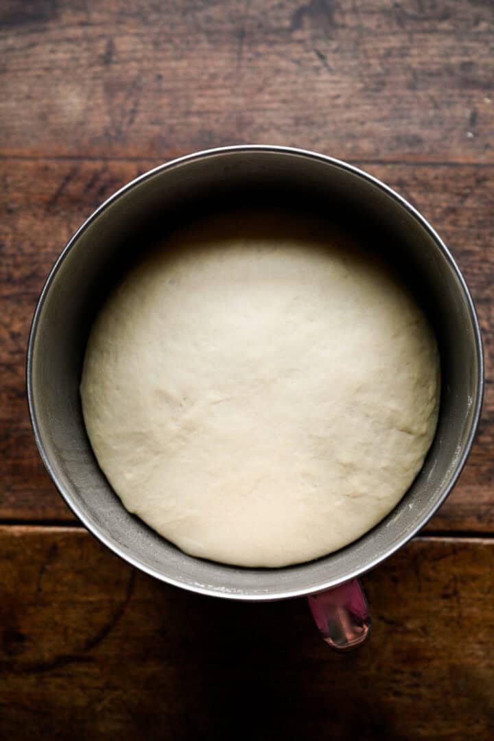Pretzel dough risen and doubled in size, filling the bottom of a stainless steel mixing bowl.