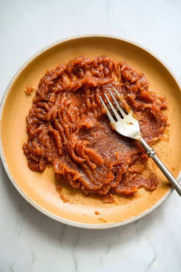 Mashed dates on a yellow plate with a fork.