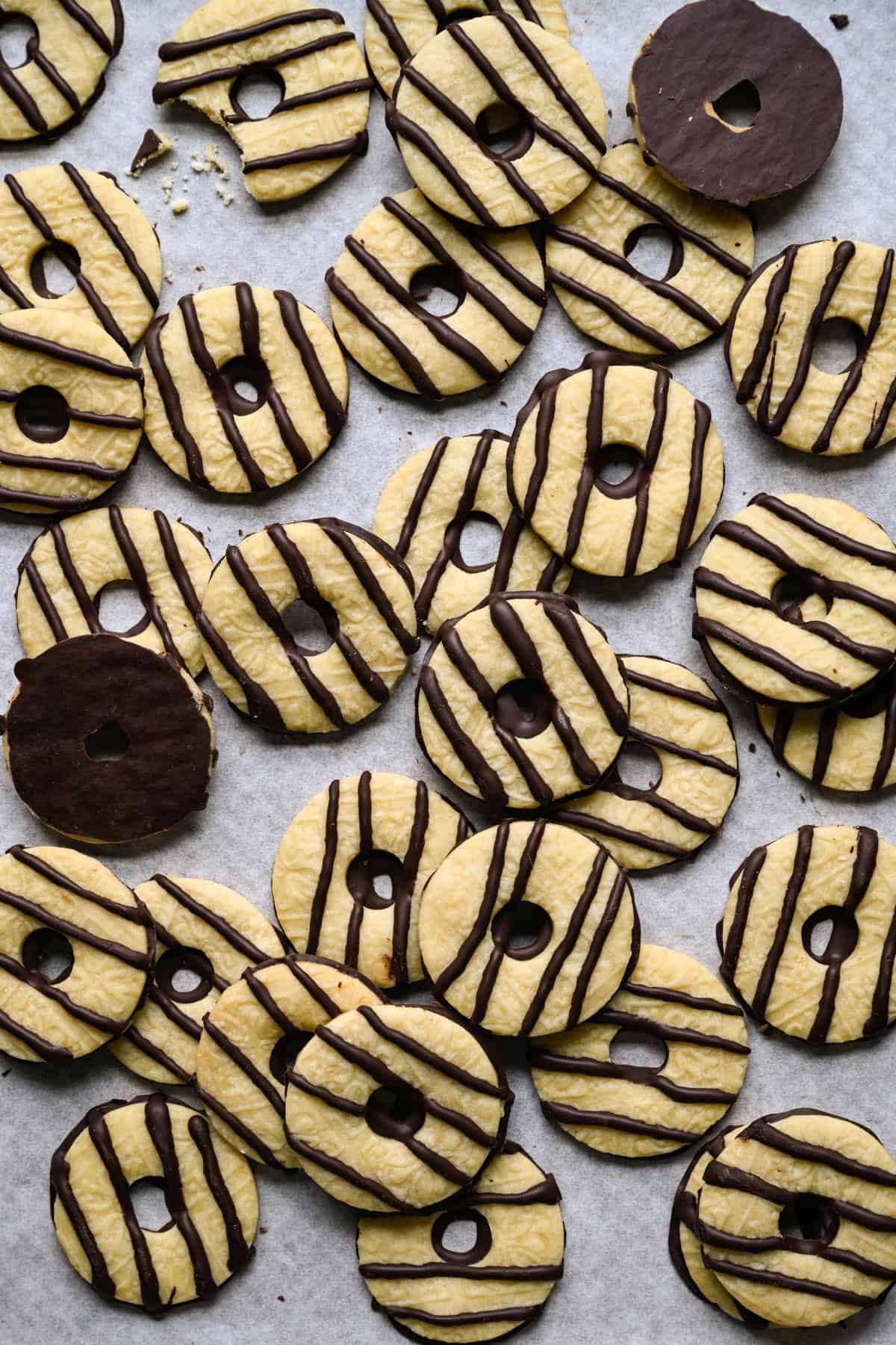 Pile of homemade fudge stripe cookies on parchment paper, with two cookies flipped over to show their chocolate-coated bottoms and one cookie with a bite taken out.