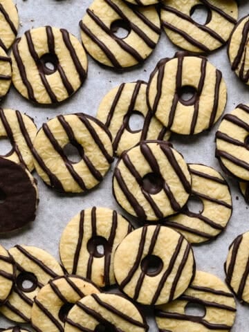 Overlapping homemade fudge stripe cookies scattered on parchment paper, with one cookie flipped over to show its chocolate-coated bottom.