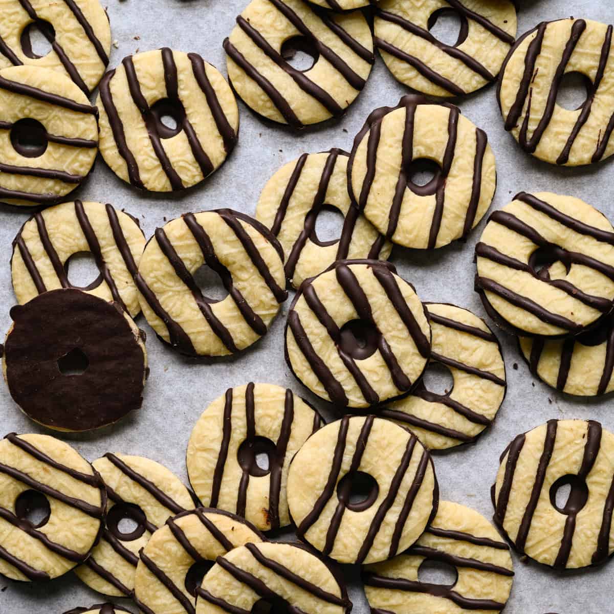 Overlapping homemade fudge stripe cookies scattered on parchment paper, with one cookie flipped over to show its chocolate-coated bottom.