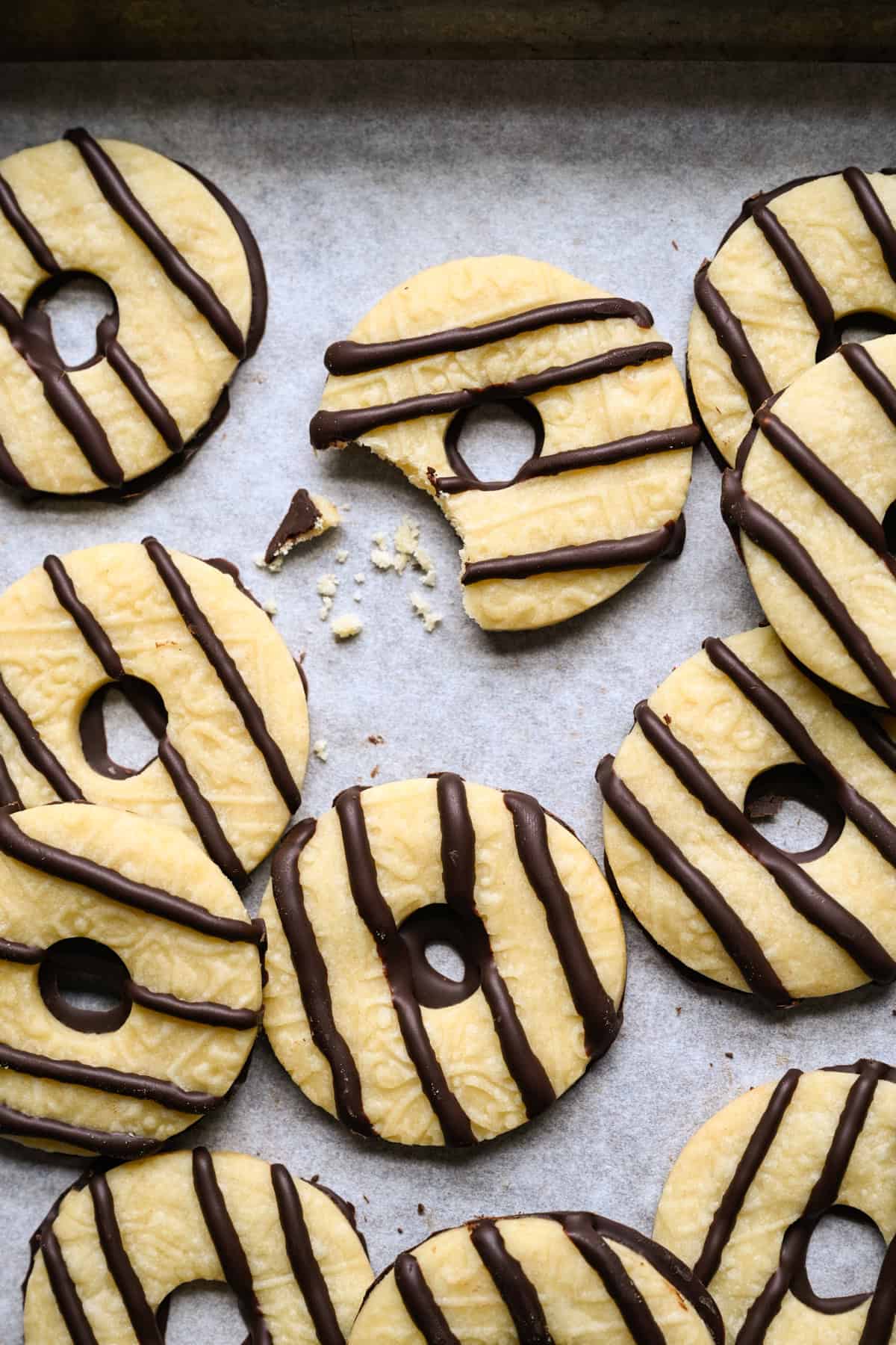 Homemade fudge stripe cookie with a bite taken out and a few crumbs beside it, surrounded by more chocolate-striped shortbread cookies on parchment paper.