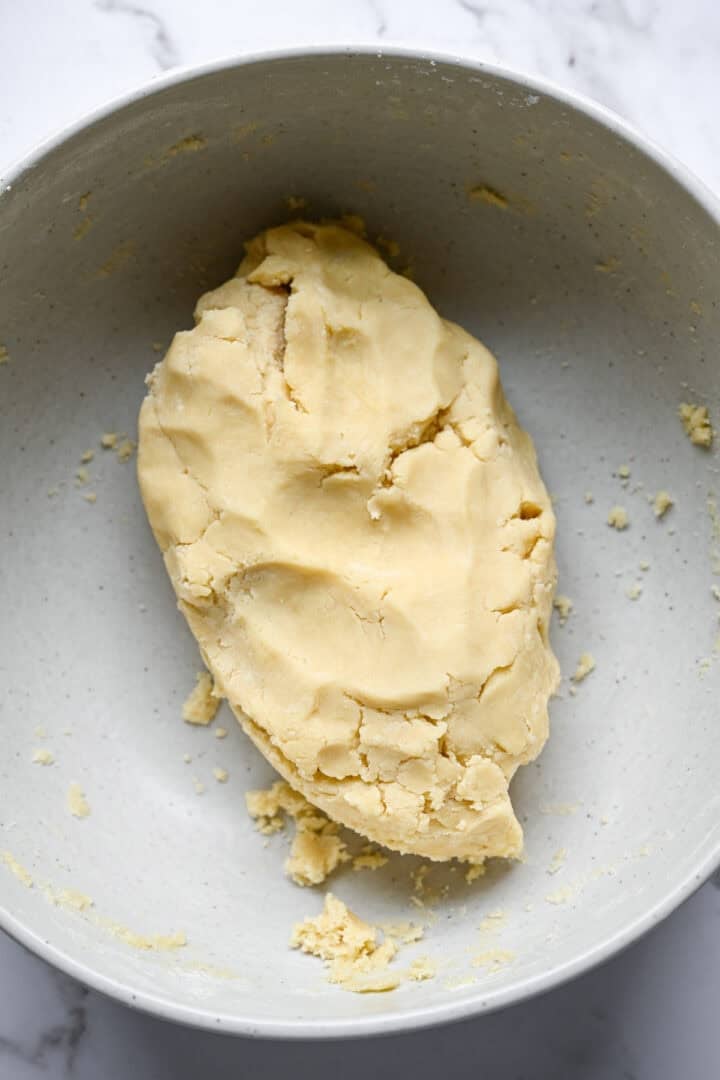 Smooth mound of shortbread cookie dough in a large speckled mixing bowl with a few crumbs around it.