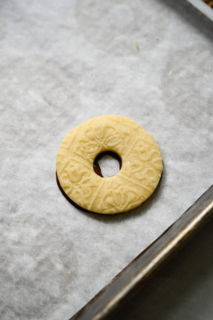 Embossed ring-shaped shortbread cookie pressed on top of a ring of melted chocolate on a parchment-lined baking sheet.