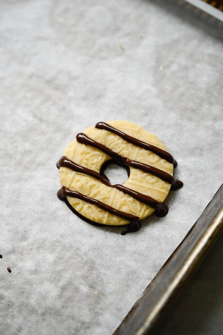 Single ring-shaped shortbread cookie with a chocolate-coated bottom and four stripes of dark chocolate drizzled across the top.
