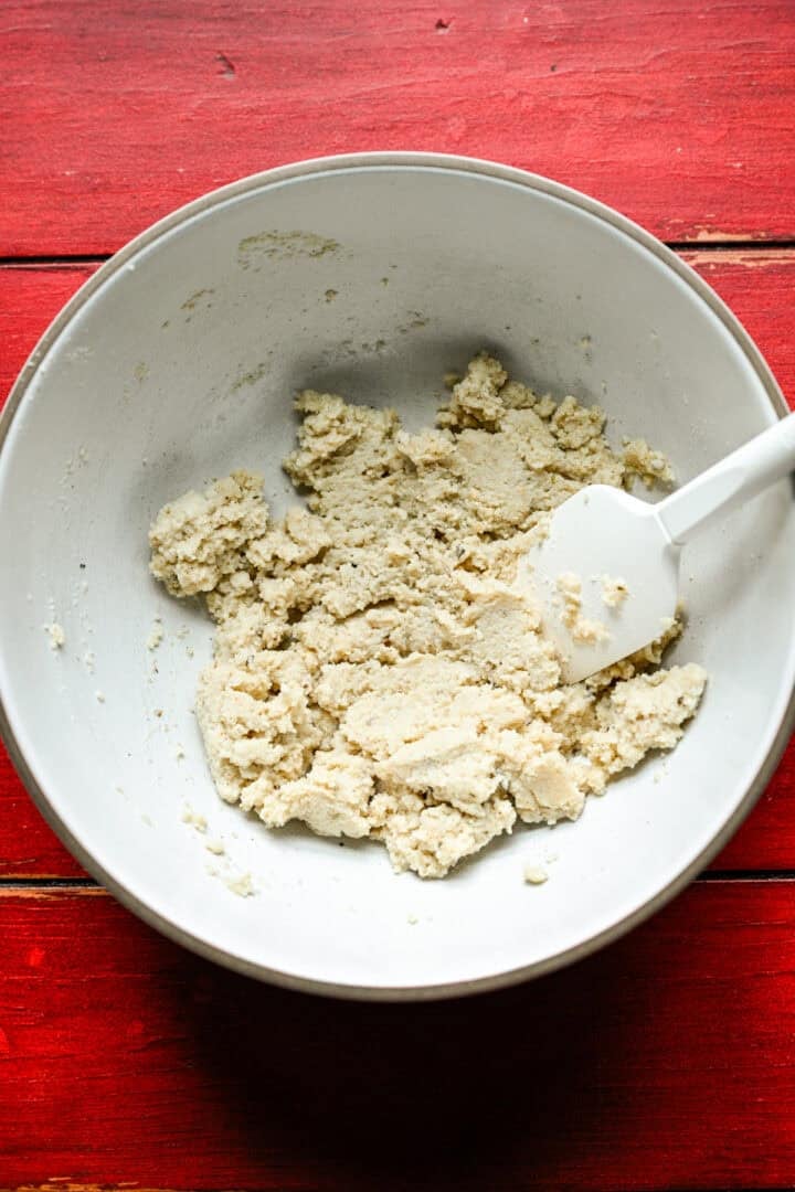 Overhead view of breadcrumbs soaked in milk to a thick paste in a white bowl with a spatula.