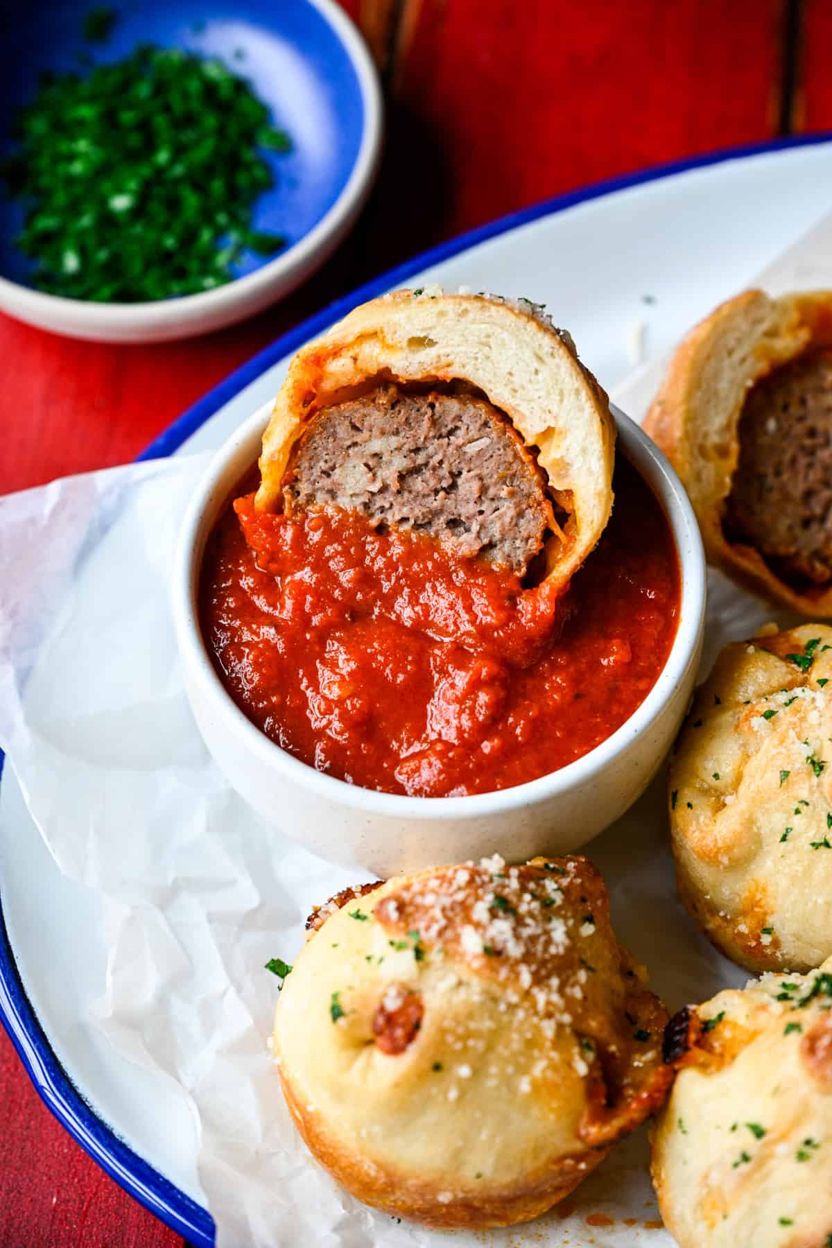 Front view of a halved meatball sub bite resting on the rim of a bowl of marinara.