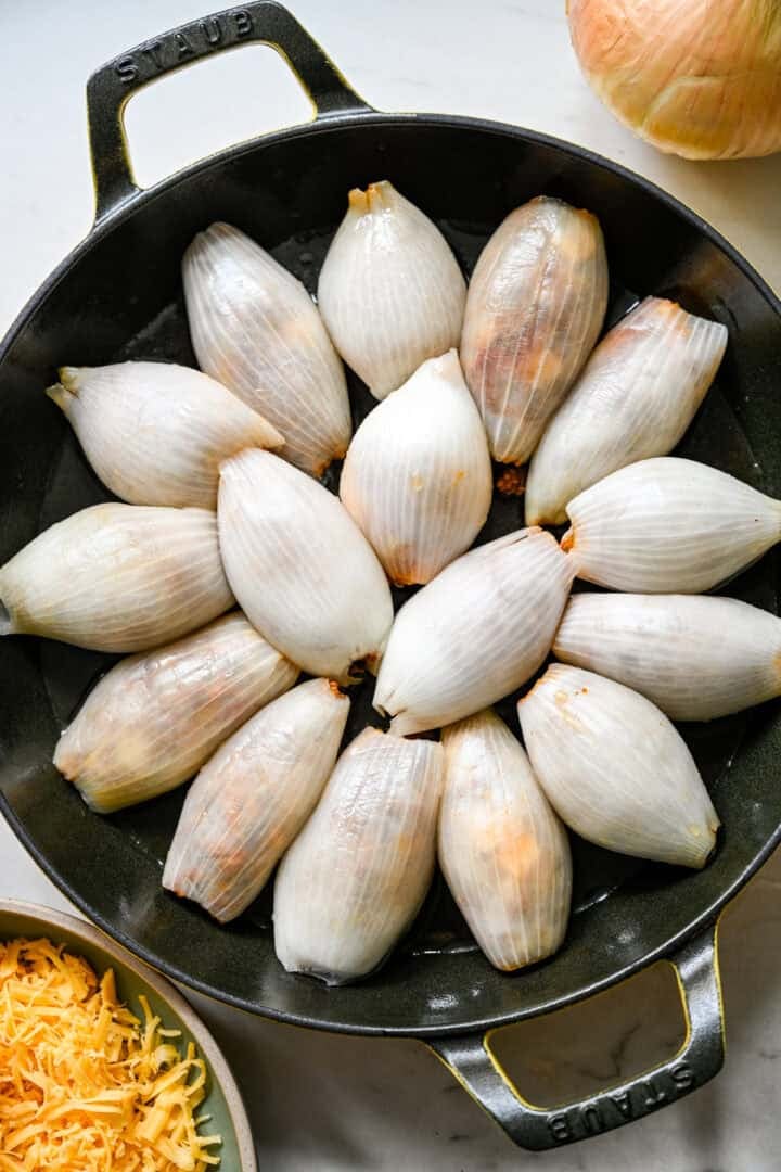 Overhead view of sixteen stuffed onion rolls arranged seam side down in a Staub cast iron skillet before baking