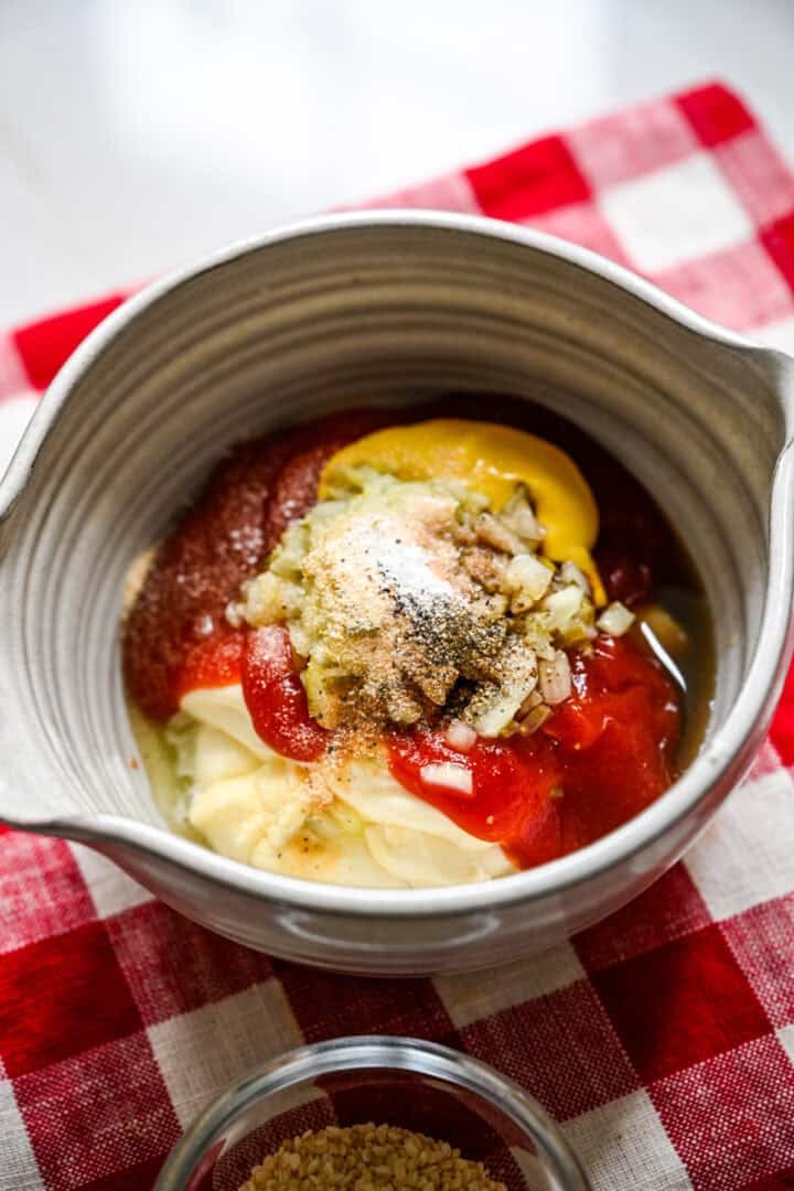 45 degree view of mayonnaise, ketchup, mustard, chopped pickles and seasonings in a gray mixing bowl for homemade Thousand Island dressing
