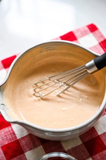 45 degree view of homemade Thousand Island dressing whisked smooth in a gray mixing bowl on a red checkered towel