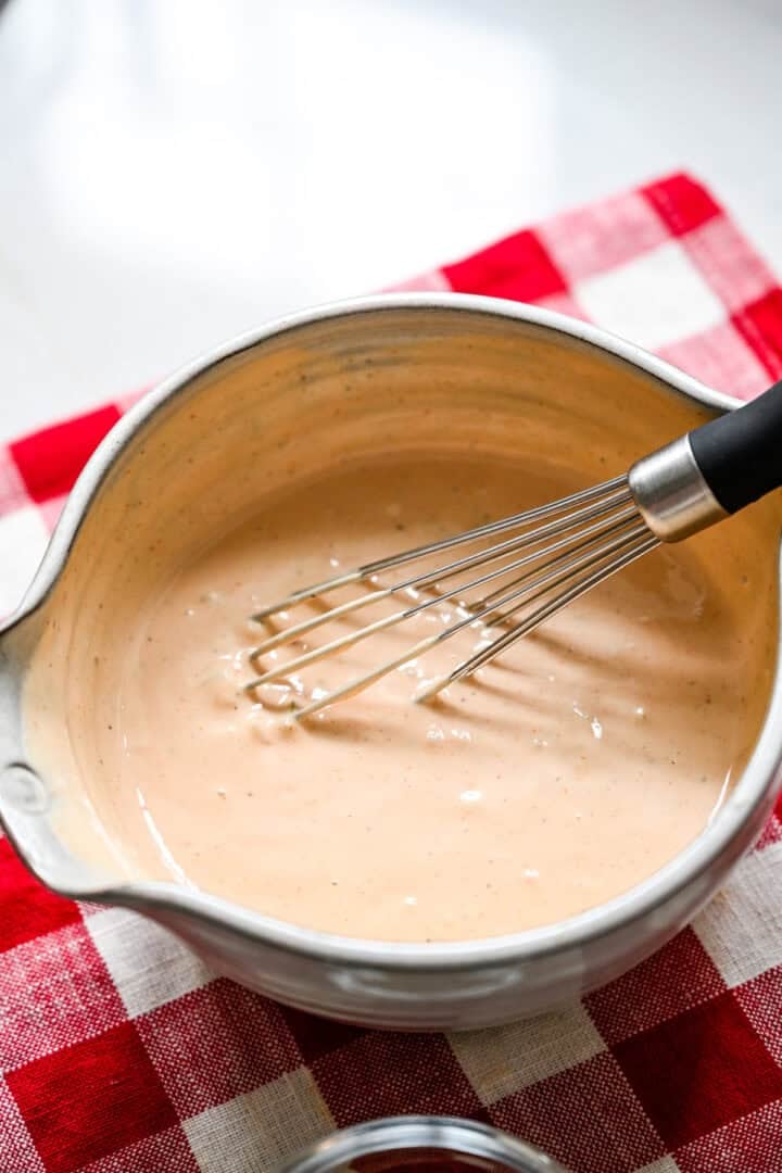45 degree view of homemade Thousand Island dressing whisked smooth in a gray mixing bowl on a red checkered towel