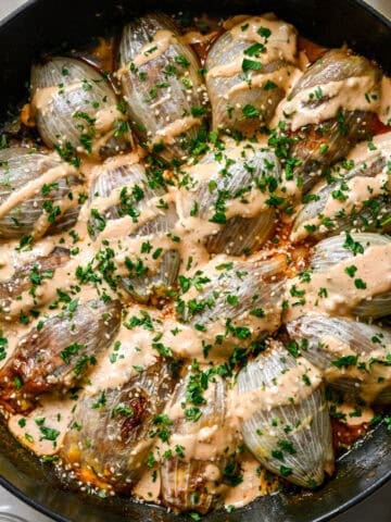 Overhead close up view of bacon cheeseburger stuffed onions in a cast iron skillet drizzled with Thousand Island and sprinkled with parsley and sesame seeds