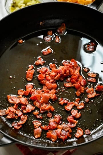 45 degree view of chopped bacon cooking until crispy in a black cast iron skillet