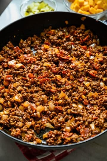 Close up view of cheeseburger filling in a cast iron skillet with ground beef, crispy bacon and diced onion stirred together