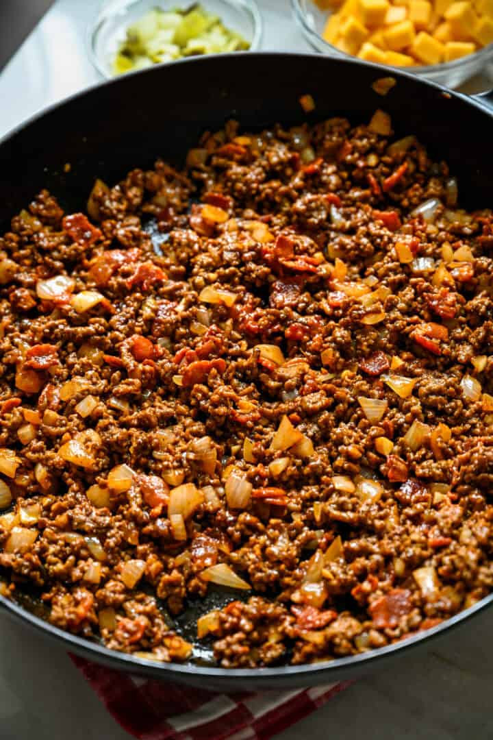 Close up view of cheeseburger filling in a cast iron skillet with ground beef, crispy bacon and diced onion stirred together