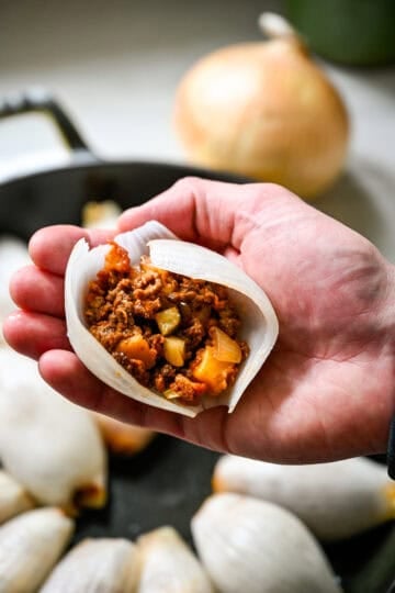 Close up view of a hand holding a boiled onion petal filled with cheeseburger filling before rolling it closed