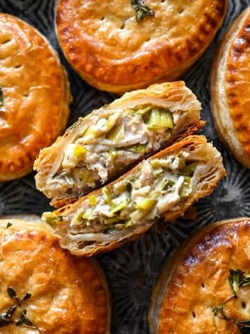 Close up overhead view of a halved chicken and leek hand pie showing the shredded chicken and leek filling inside flaky puff pastry, with whole pies around it.