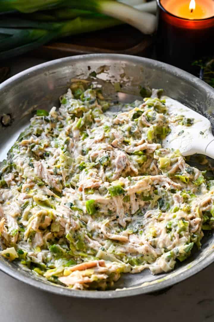 45 degree view of the finished creamy chicken and leek filling in a skillet, stirred together with a white spatula.