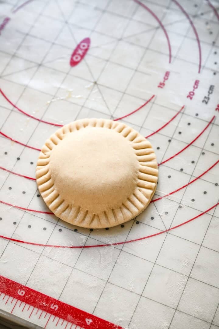 Close up view of one assembled, unbaked hand pie with fork-crimped edges on an OXO pastry mat.