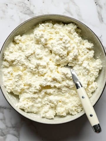 Overhead view of creamy homemade cottage cheese in a bowl with a spoon stirring in heavy cream