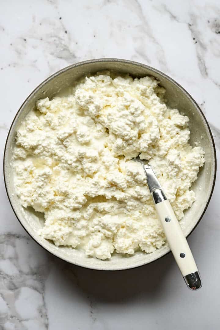 Overhead view of a bowl of homemade cottage cheese with a spoon on a marble counter