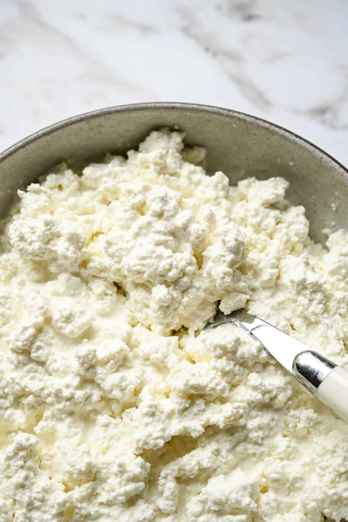 Close up view of creamy homemade cottage cheese curds in a bowl with a spoon