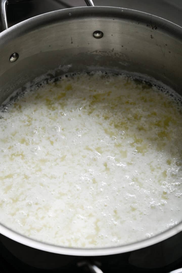 45 degree view of milk separating into curds and whey in a stainless steel pot after adding vinegar