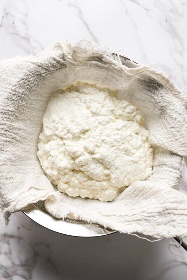 Overhead view of fresh cottage cheese curds draining in a cheesecloth-lined strainer