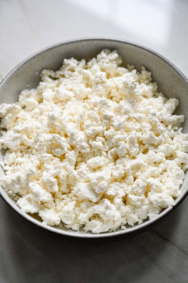 45 degree view of drained homemade cottage cheese curds in a stoneware bowl before adding cream