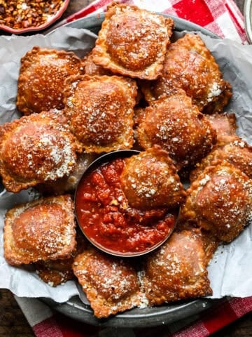 A platter piled with crispy homemade pizza rolls topped with grated parmesan, with one dipped into a small bowl of pizza sauce.