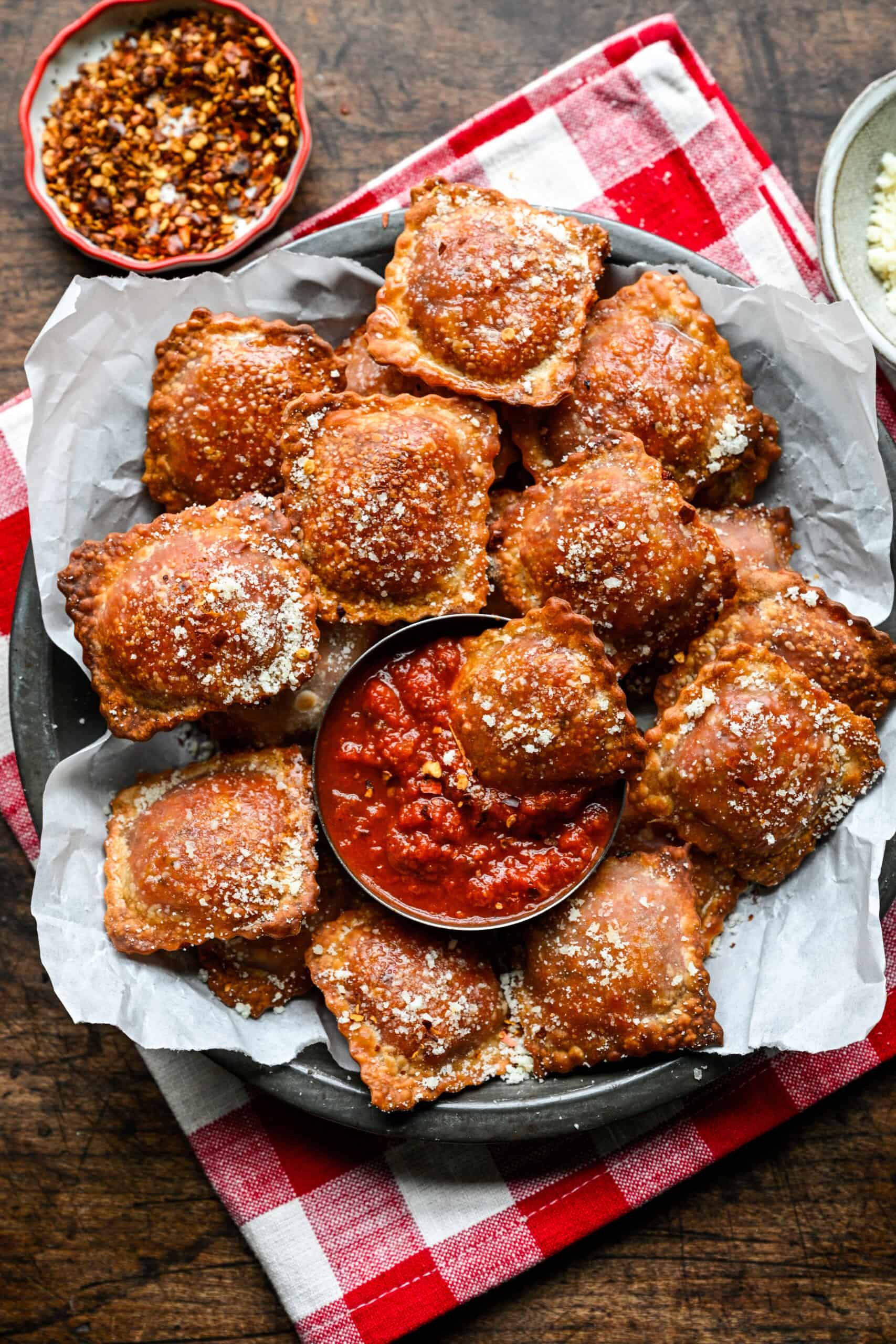 Homemade pizza rolls on a parchment-lined plate set on a red and white checkered napkin, with one pizza roll dipped in pizza sauce.